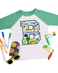 Green-sleeve kids raglan tee with a playful school-themed “B” design for Blue Sage Elementary, decorated with colorful doodles like books, a school bus, sports balls, trees, and pencils. Surrounded by vibrant school supplies, sunglasses, and toys for a fun flat lay presentation.