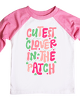 A kids’ St. Patrick’s Day shirt with pink raglan sleeves and a playful design featuring the phrase “Cutest Clover in the Patch” in fun, colorful lettering with green shamrock accents. The shirt is perfect for festive holiday outfits, adding a cheerful touch of Irish charm.