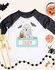 Children's Halloween-themed shirt with ghost design and name 'Colsen', surrounded by Halloween decorations.