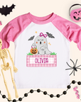 Pink and white t-shirt with ghost design and 'Olivia' text, surrounded by Halloween decorations.