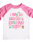Pink and white raglan shirt featuring the festive phrase 'I run on cookies & Christmas cheer' in playful pink, green, and red lettering, surrounded by holiday-themed elements like stars, a Christmas tree, and a gingerbread man.