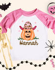 Pink and white Halloween-themed shirt with a pumpkin design and skeleton, surrounded by Halloween decorations.
