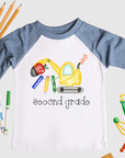 Children's shirt with an excavator graphic and 'second grade' text, surrounded by school supplies on a white background.
