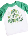 A Wee Little Hooligan Shirt featuring a playful St. Patrick’s Day design with green and gold typography, shamrocks, stars, and a leprechaun hat. The white and blue raglan tee is paired with denim jeans and festive accessories, including gold coins, shamrock beads, and four-leaf clovers, creating a fun and lucky holiday outfit for kids.