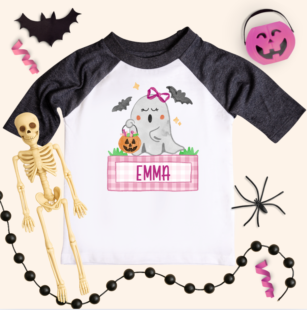 Halloween-themed children's shirt with ghost design and name 'Emma', surrounded by Halloween decorations.