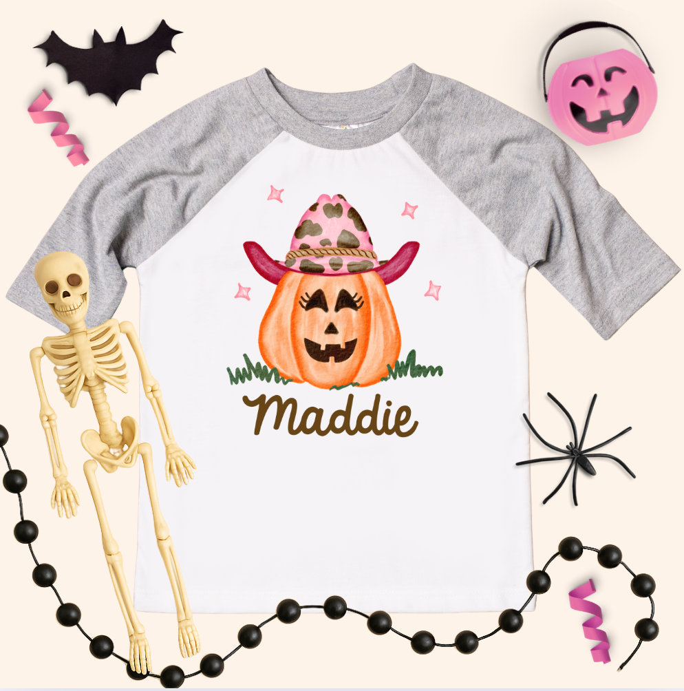 Halloween-themed t-shirt with pumpkin and cowboy hat design, surrounded by Halloween decorations.