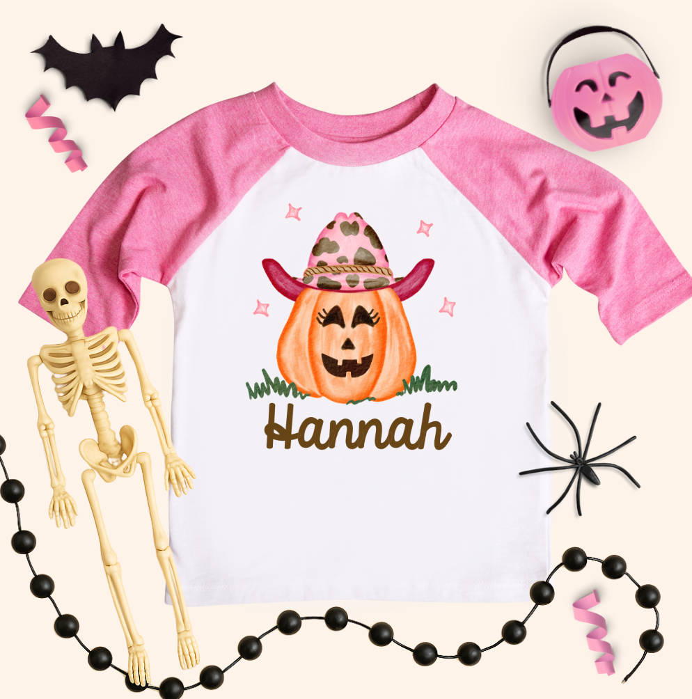 Pink and white Halloween-themed shirt with a pumpkin design and skeleton, surrounded by Halloween decorations.