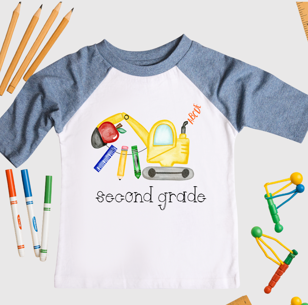 Children's shirt with an excavator graphic and 'second grade' text, surrounded by school supplies on a white background.